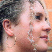 A model wearing one large hoop earring made of sterling silver with gold verneil.