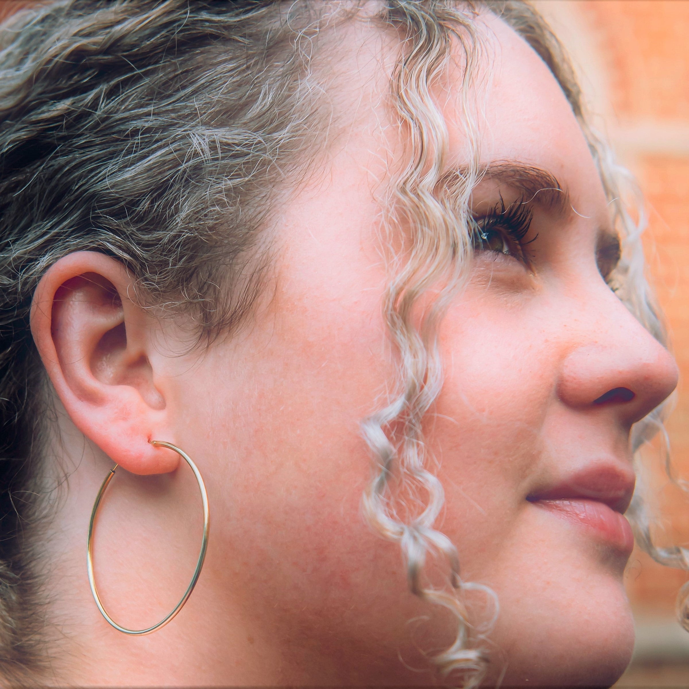 A model wearing one large hoop earring made of sterling silver with gold verneil.