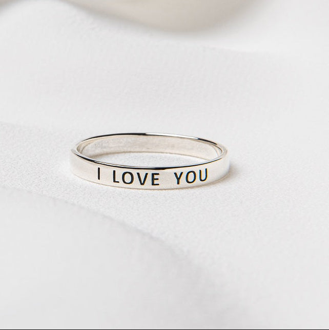 A silver ring with the inscription 'I love you' displayed on it, placed on a white fabric surface.