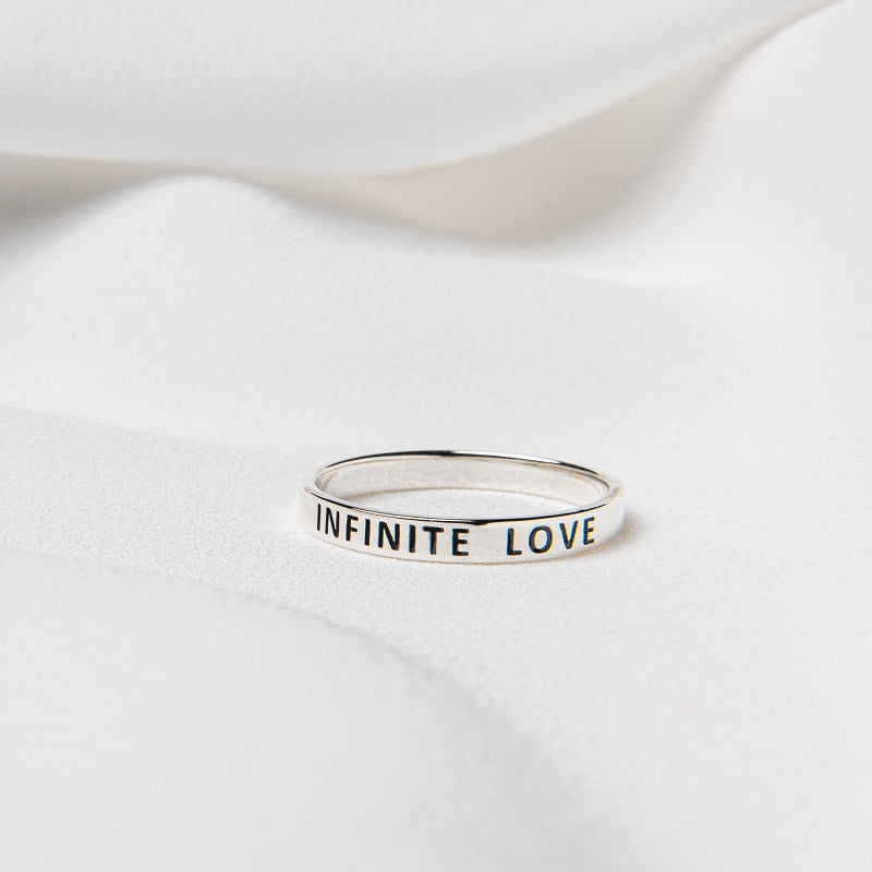 A silver ring with the words "INFINITE LOVE" inscribed on the band on a white surface.