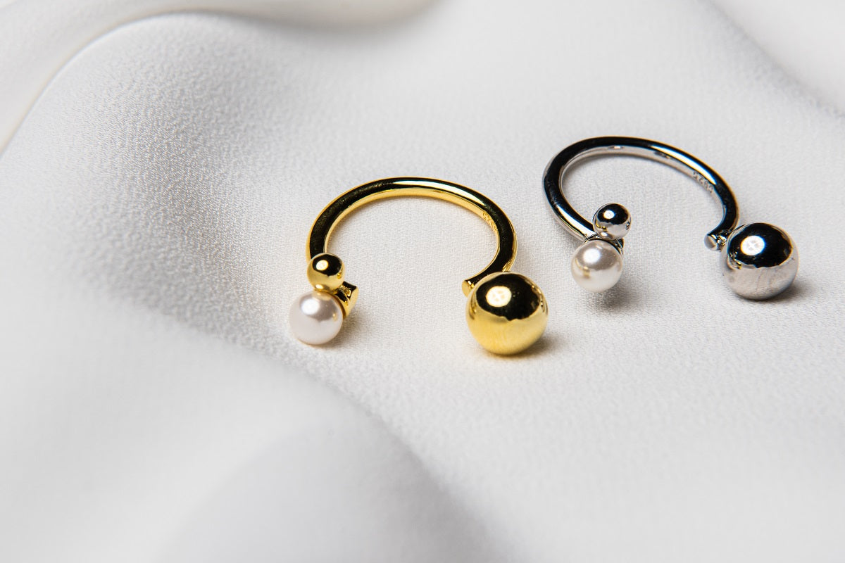 A polished silver ring and a polished gold ring with three spherical embellishments on a white fabric background.