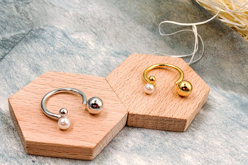 A polished silver ring and a polished gold ring with three spherical embellishments on a wooden display