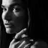 Black and white close up of a models hand wearing a black ring infront of her face