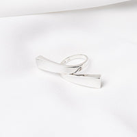 A polished silver ring with a knot design, displayed on a white surface.