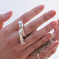 Silver ring in a knot design displayed on a model's hand which is holding beach sand