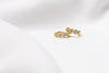 A pair of gold vermeil huggies earrings with leaf patterns with cubic zirconia stones, displayed on a white satin background.