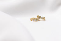 A pair of gold vermeil huggies earrings with leaf patterns with cubic zirconia stones, displayed on a white satin background.
