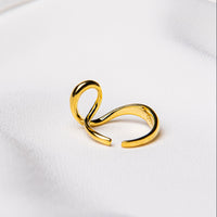 A gold ring with a flowing design on a white fabric background
