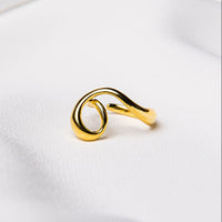 A gold ring with a flowing design on a white fabric background