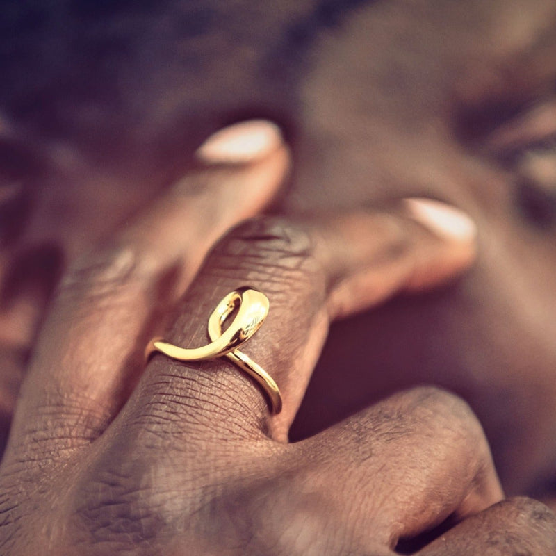 A close up of a woman wearing a gold ring with a flowing design