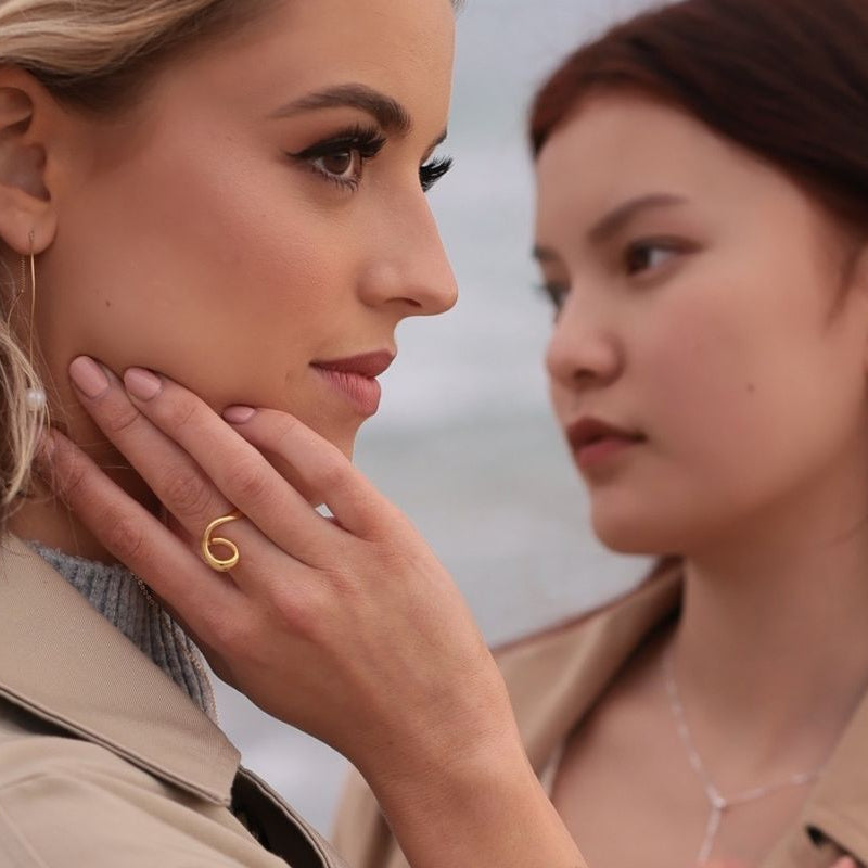 A close up of a womanwearing a gold ring with a flowing design