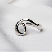 A silver ring with a flowing design on a white fabric background