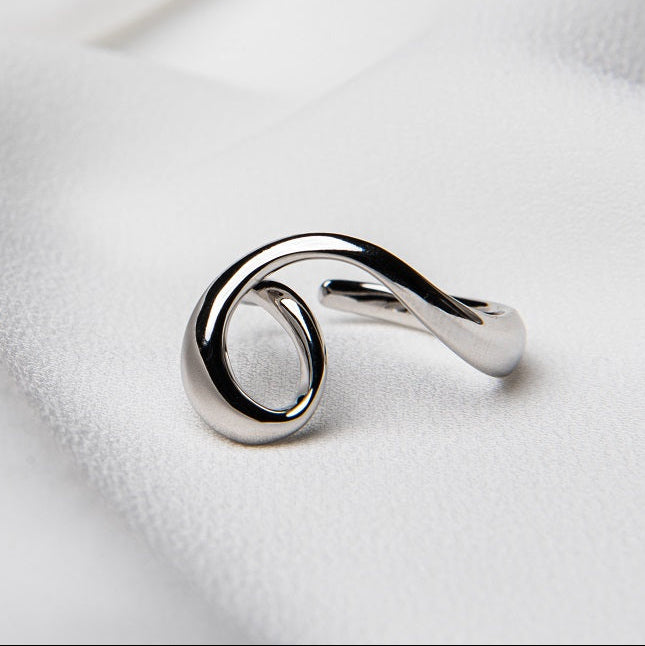 A silver ring with a flowing design on a white fabric background