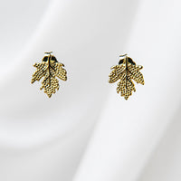 A pair of maple leaf-shaped stud earrings with a gold vermeil finish on a white silky background.