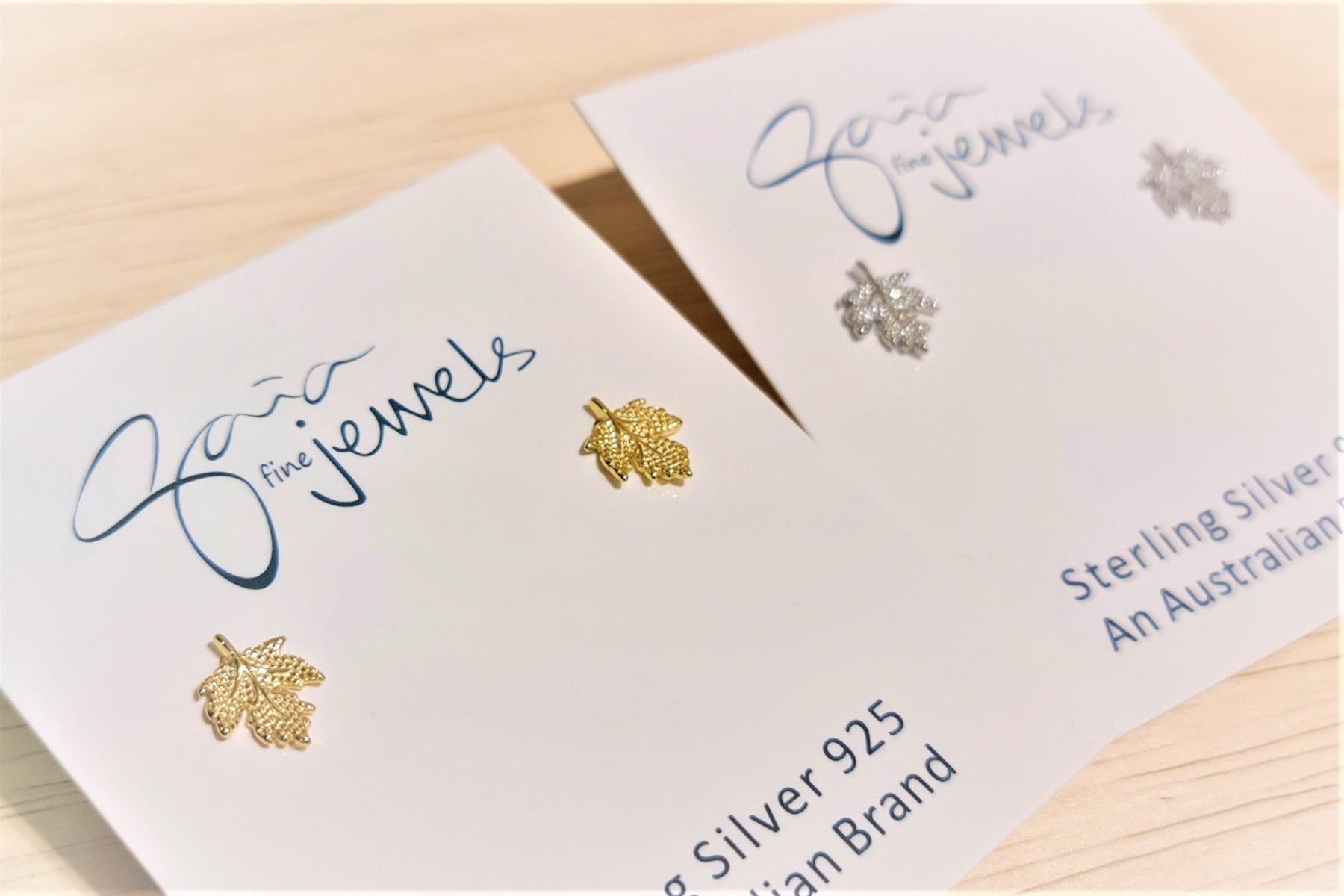 two pairs of maple leaf earrings  one gold and one silverm featured on an earring card.