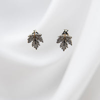 A pair of maple leaf-shaped stud earrings with a gold vermeil finish on a white silky background.