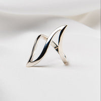 A polished, silver-colored ring with a smooth, curved design, displayed on a white fabric background.