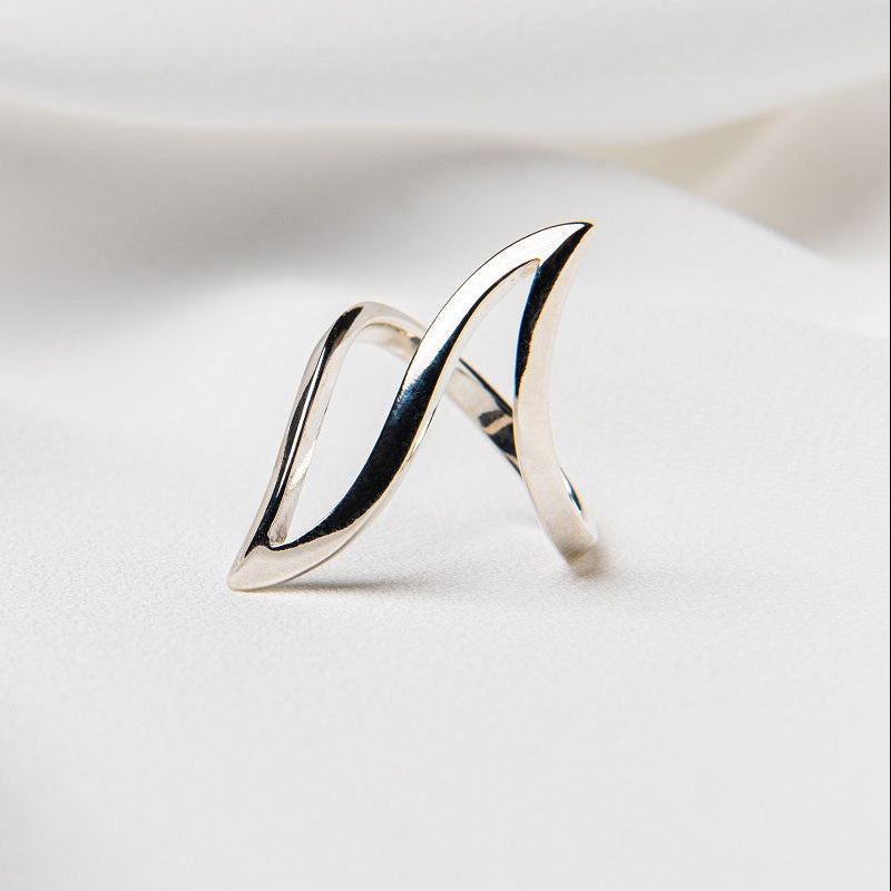 A polished, silver-colored ring with a smooth, curved design, displayed on a white fabric background.