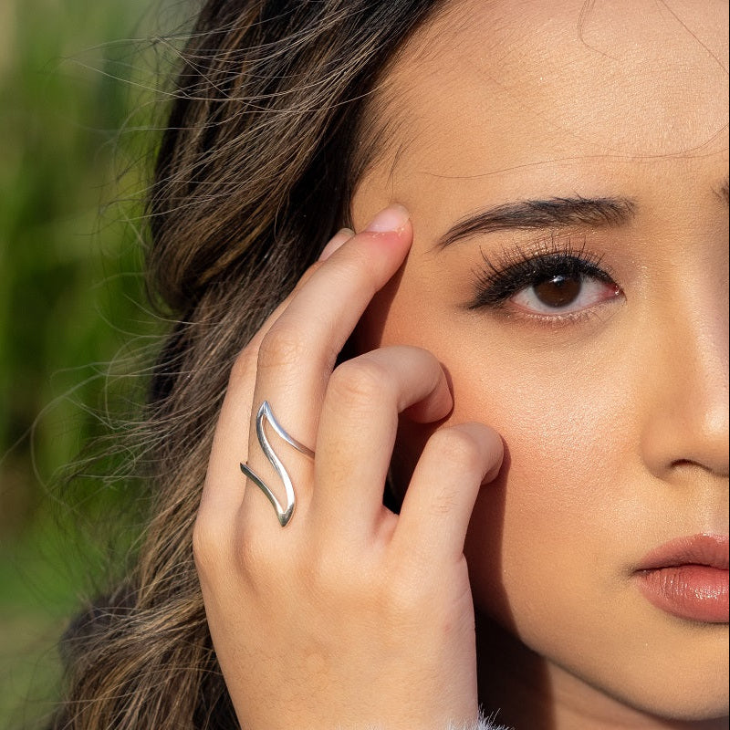 A close up  of a model wearing a silver ring in the shape of a flowing wave.