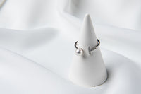 A silver ring featuring a pearl and cubic zirconias on a white display