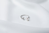 A silver ring featuring a pearl and cubic zirconias on a white cloth