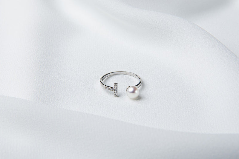 A silver ring featuring a pearl and cubic zirconias on a white cloth