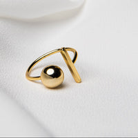 Close up of a gold vermeil ring featuring a bar and a ball on a white fabric background.