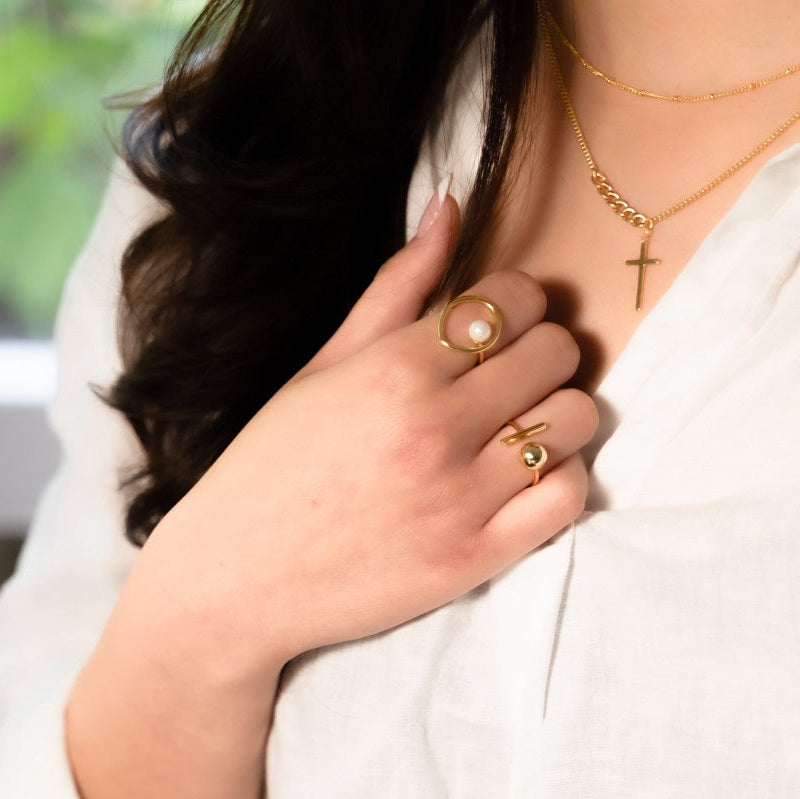 A woman wearing a gold ring featuring a bar and a ball.