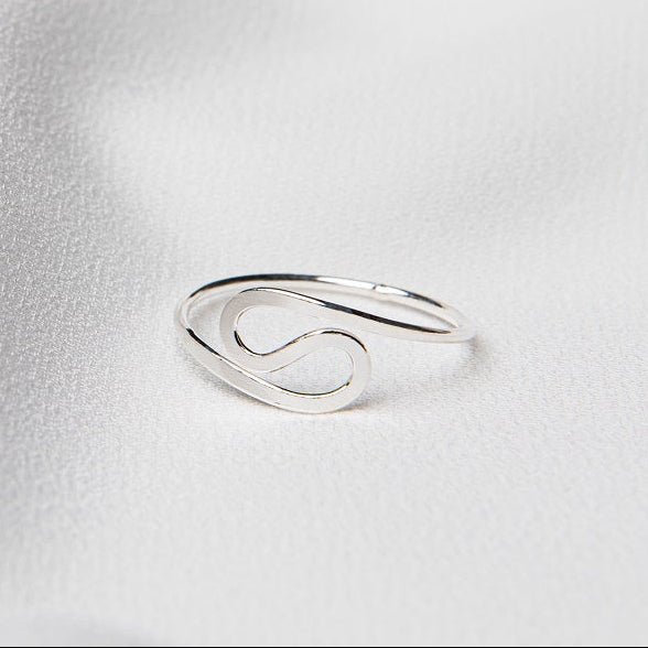A polished silver adjustable ring on a white silky surface