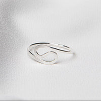 A polished silver adjustable ring on a white silky surface