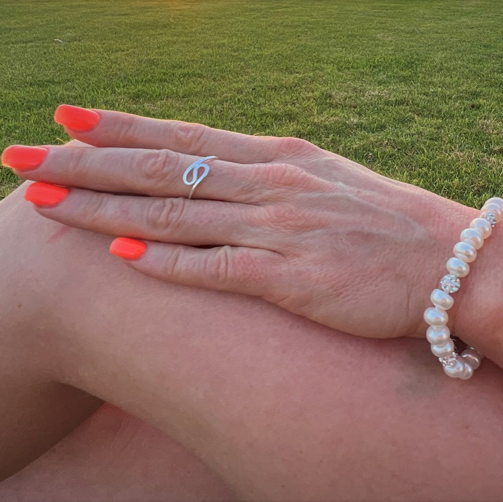 A close up of a womans hand wearing a silver ring in the shape of a wave
