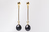 A pair of black pearl earrings with gold dangle components and butterfly backs, displayed against a white background.