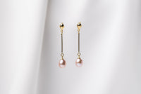 A pair of pearl earrings with gold vermeil  clasps and butterfly backs, displayed against a white fabric background.