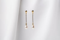 A pair of pearl earrings with a gold vermeil dangle design and butterfly backs, displayed against a white fabric backdrop.