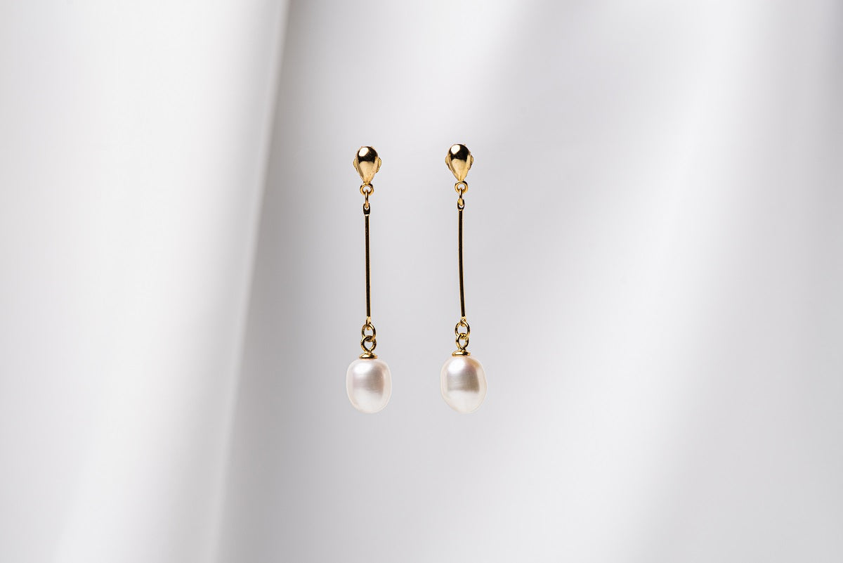 A pair of pearl earrings with a gold vermeil dangle design and butterfly backs, displayed against a white fabric backdrop.