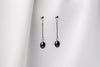A pair of dark blue pearl earrings with a silver dangle design and butterfly backs, displayed against a white fabric backdrop.
