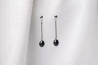 A pair of dark blue pearl earrings with a silver dangle design and butterfly backs, displayed against a white fabric backdrop.