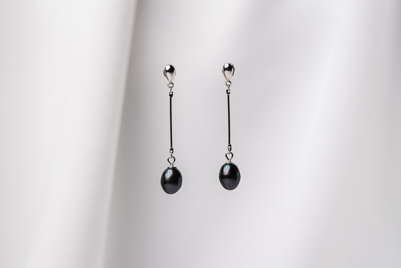 A pair of dark blue pearl earrings with a silver dangle design and butterfly backs, displayed against a white fabric backdrop.
