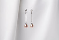 A pair of rose pearl earrings with dangle and drop shapes, featuring butterfly backs, displayed against a white fabric backdrop.