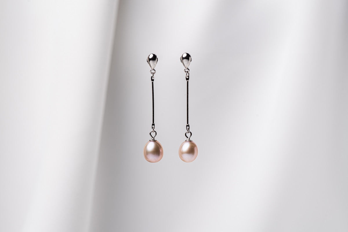 A pair of rose pearl earrings with dangle and drop shapes, featuring butterfly backs, displayed against a white fabric backdrop.
