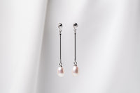 A pair of pearl earrings with a silver dangle design and butterfly backs, displayed against a white fabric backdrop.