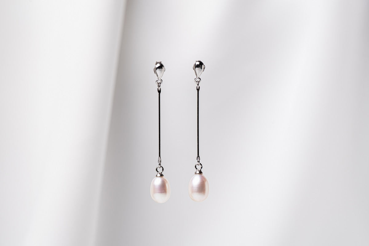 A pair of pearl earrings with a silver dangle design and butterfly backs, displayed against a white fabric backdrop.