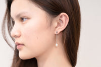 A pair of pearl earrings with silver clasps and butterfly backs, worn by a woman model.