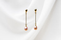 A pair of rose pearl earrings with a gold vermeil dangle design and butterfly backs, displayed against a white fabric backdrop.