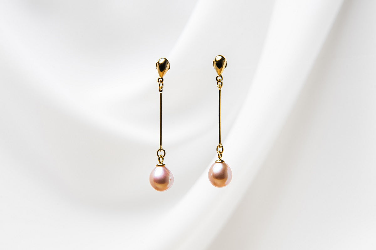 A pair of rose pearl earrings with a gold vermeil dangle design and butterfly backs, displayed against a white fabric backdrop.