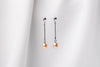 A pair of champaigne pearl earrings with a silver dangle design and butterfly backs, displayed against a white fabric backdrop.