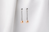 A pair of champaigne pearl earrings with a silver dangle design and butterfly backs, displayed against a white fabric backdrop.