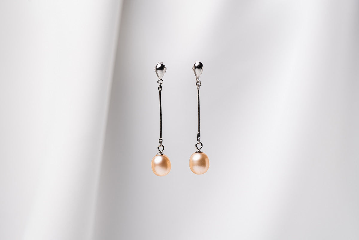 A pair of champaigne pearl earrings with a silver dangle design and butterfly backs, displayed against a white fabric backdrop.