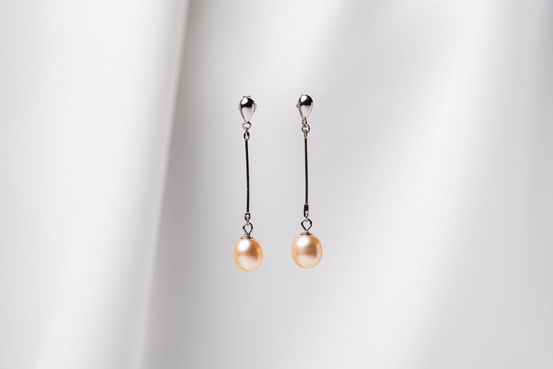 A pair of champaigne pearl earrings with a silver dangle design and butterfly backs, displayed against a white fabric backdrop.