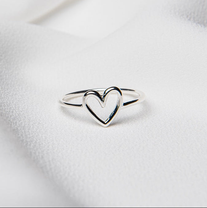 A polished sterling silver ring with an open heart design, displayed on a white surface.